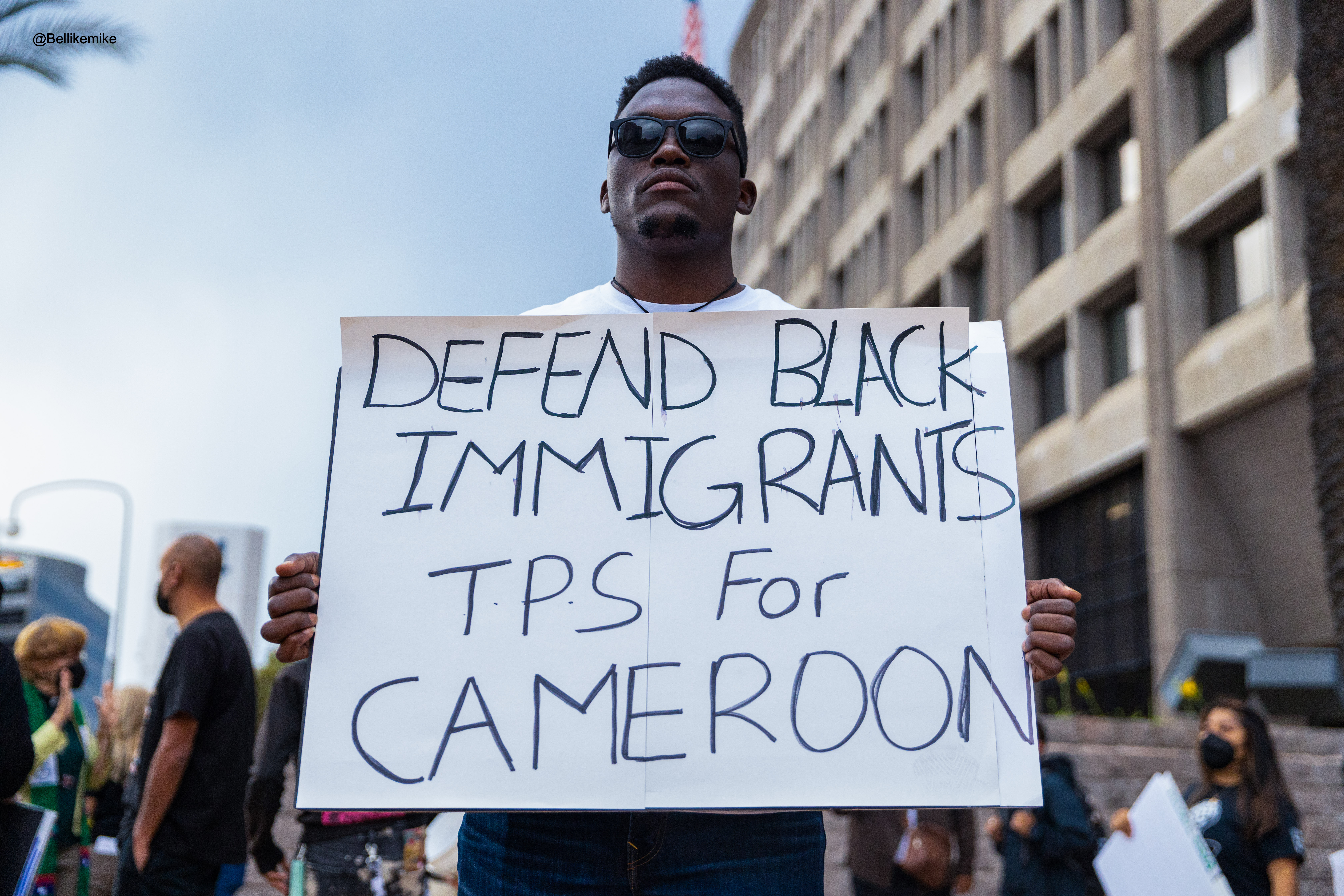 protestor holds sign: defend black immigrants tps for cameroon
