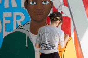 Student artist works on mural wall