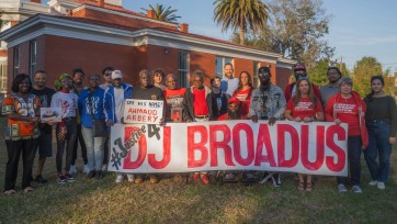 A group of people standing in front of a building, holding a sign that says "Justice for DJ Bradus."