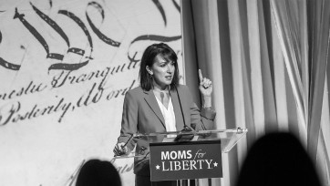A woman giving a speech at a podium with a sign that says "Moms of Liberty."