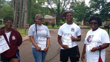 Four people hold clipboards with voting registration forms