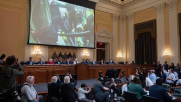 Video plays on screen above congressional panel meeting