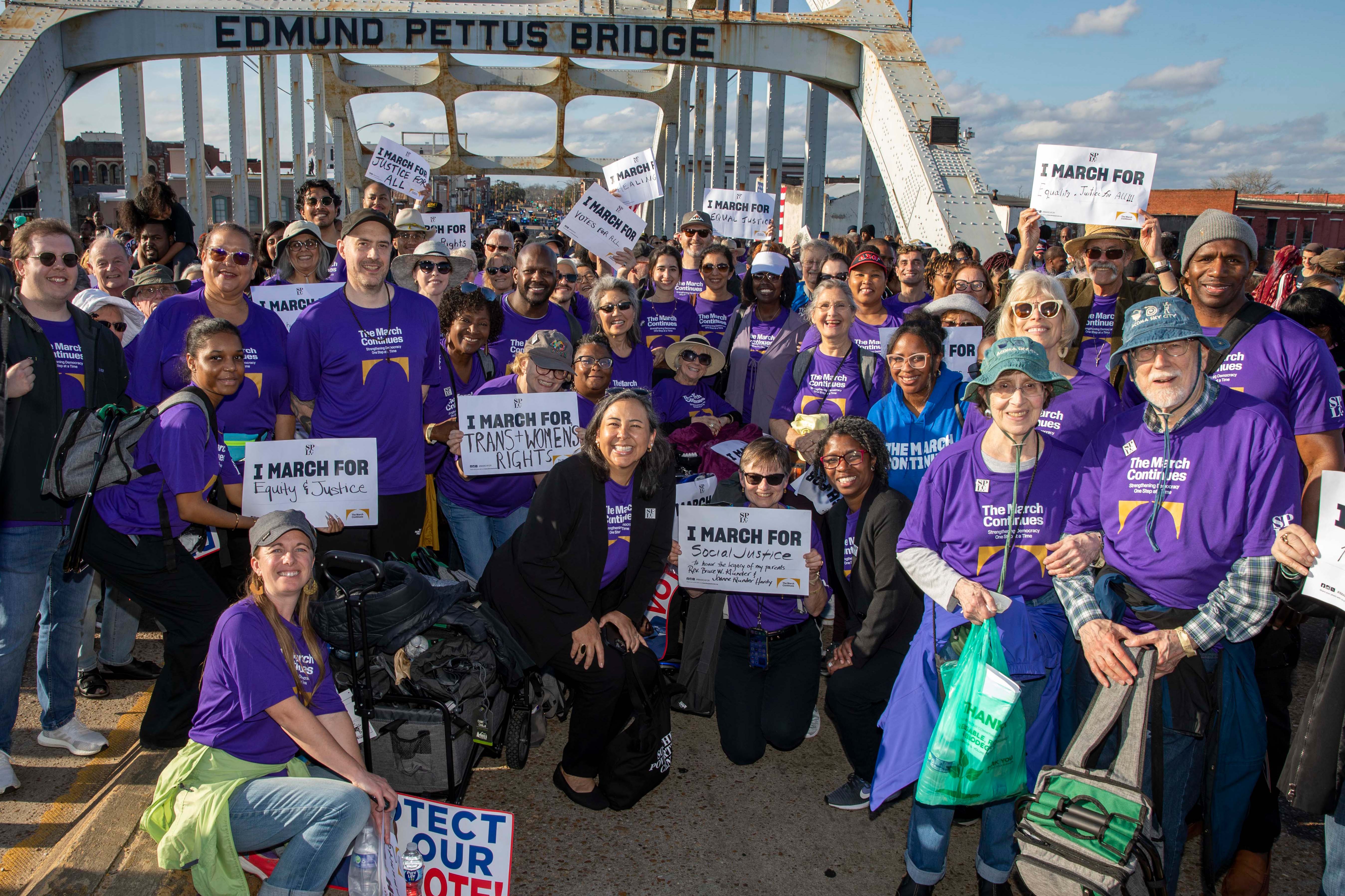 Group of people in purple shirts gathered under bridge arch.