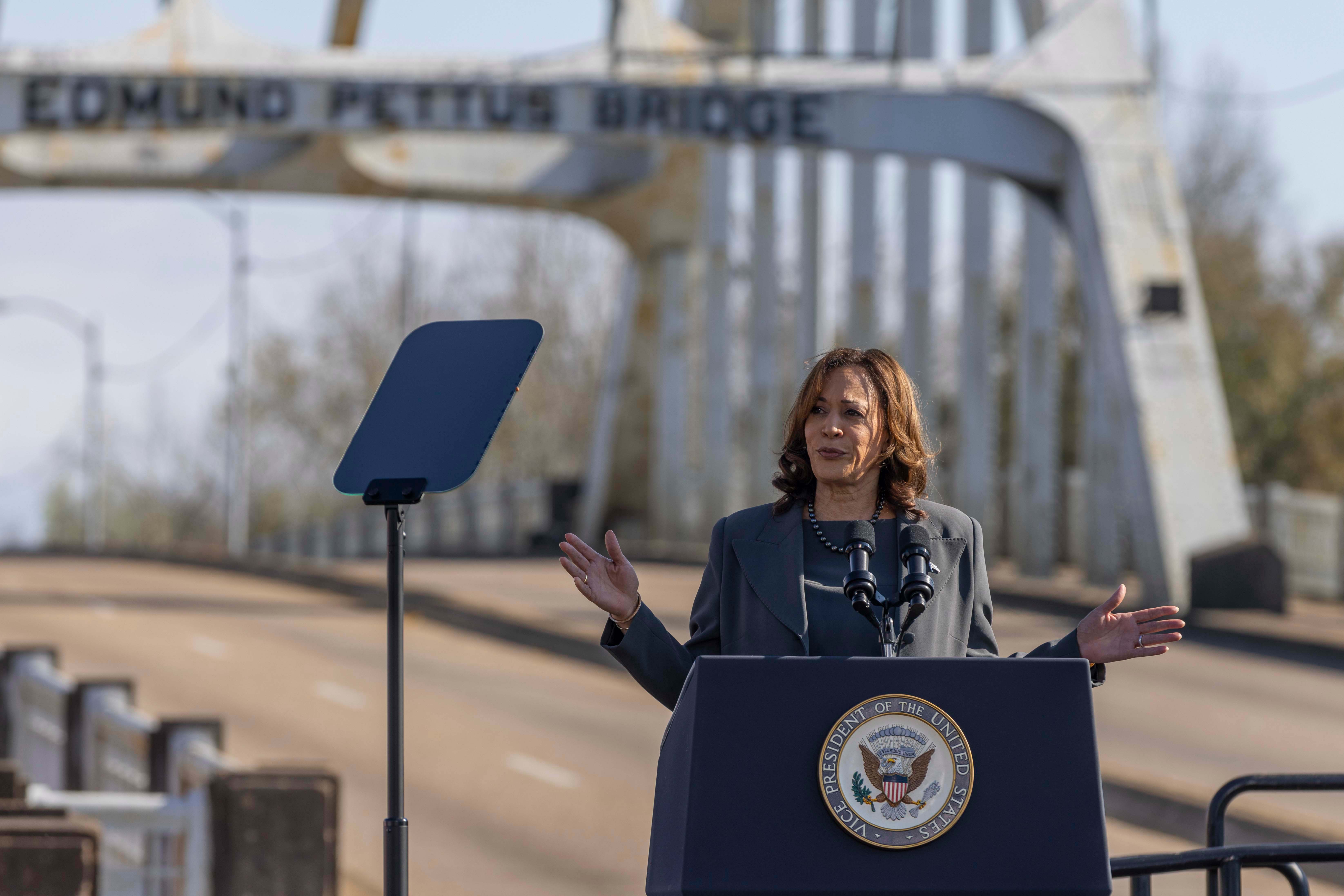 Kamala Harris at podium with Edmund Pettus Bridge in background.