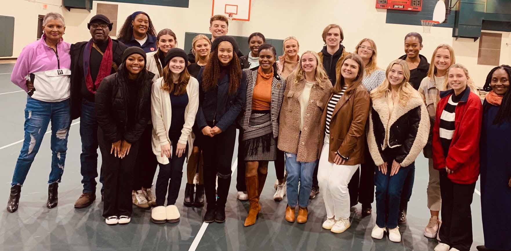auburn-university-clotilda Two rows of nearly two dozen people lined up for a photo inside a gymnasium.