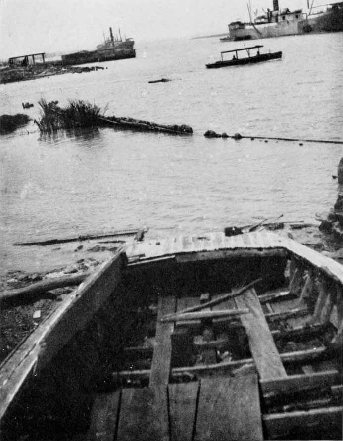 clotilda-remnants Up close black and white image of boat on a muddy shore as another boat floats on water in background.