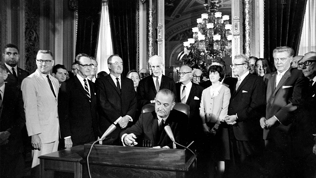 President Lyndon B. Johnson is surrounded by people as he signs law