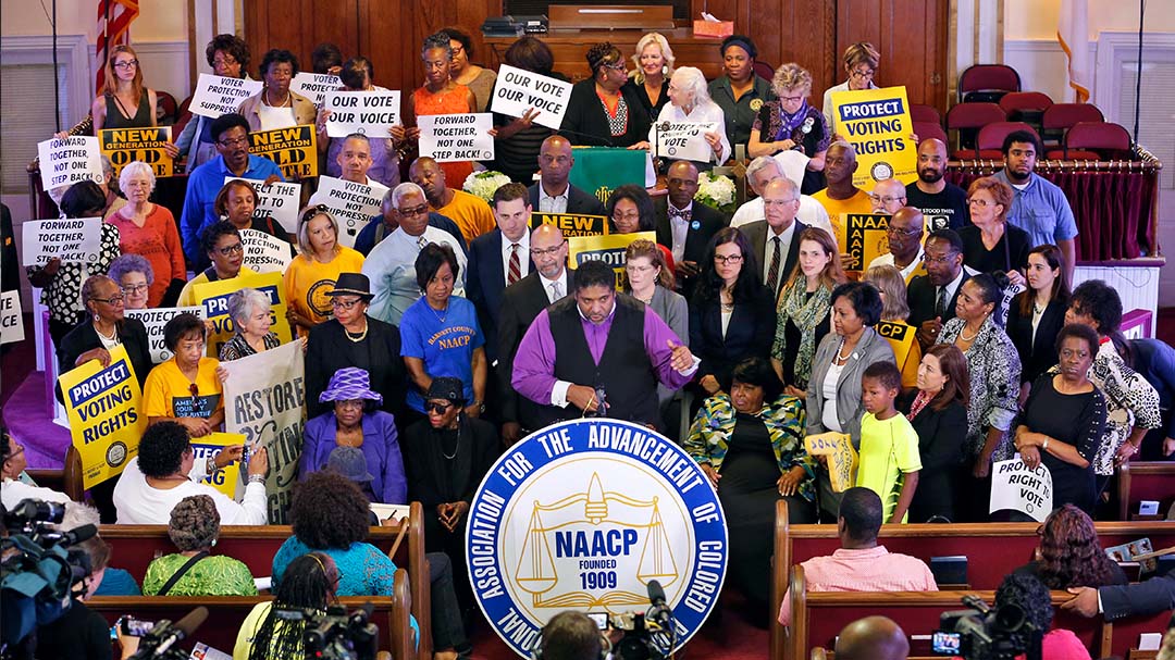 William Barber at podium surrounded by numerous people