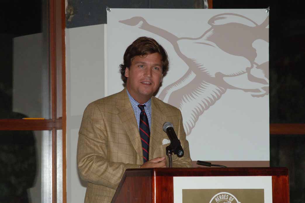 Tucker Carlson dressed in suit and tie at a podium