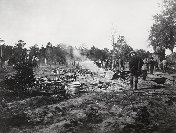 People stand around burned remains of house