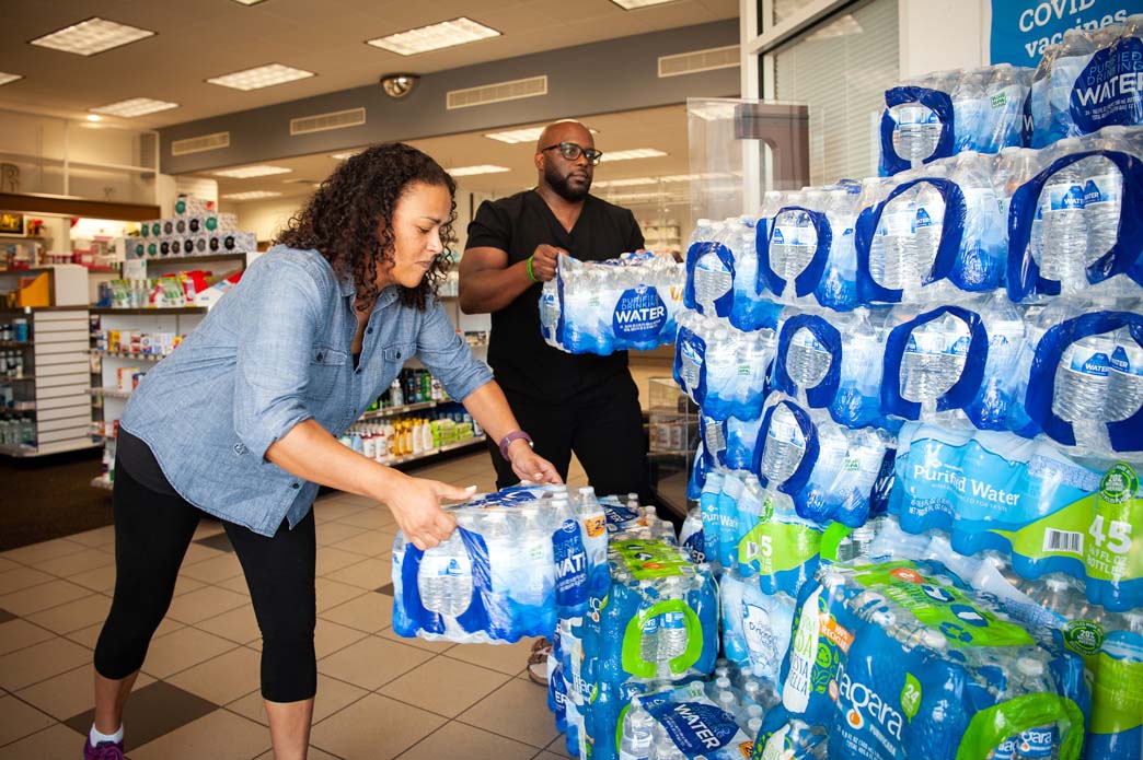 Two people collect cases of water bottles inside grocery store