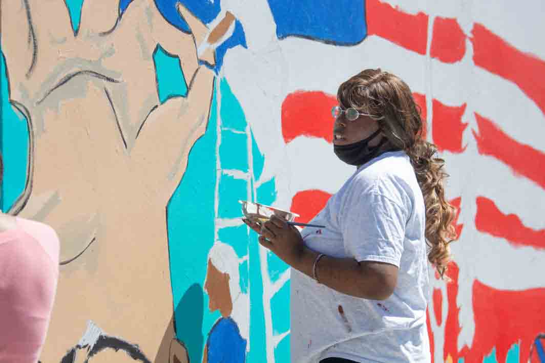 Student artist works on mural wall
