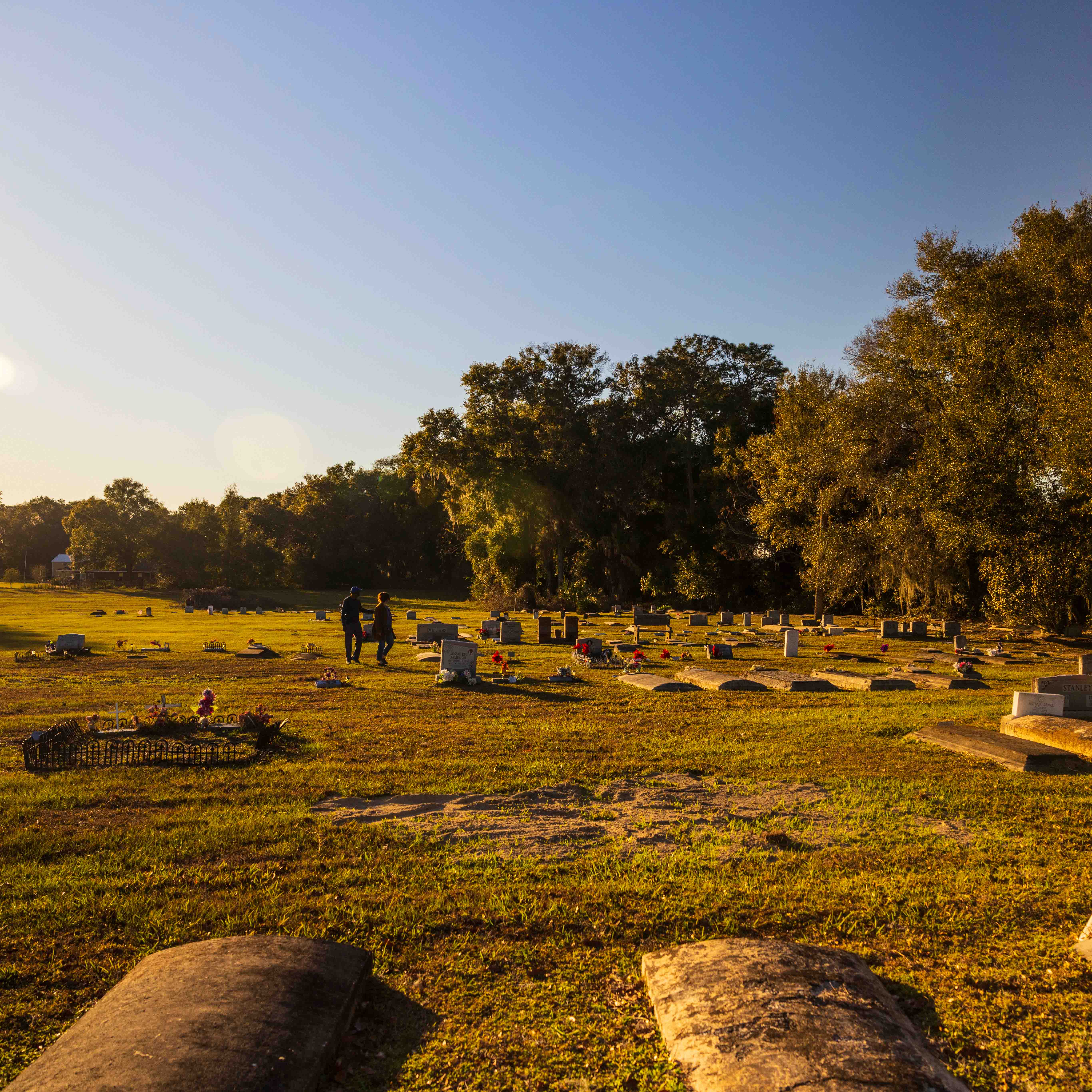 Two people walk in a field of cemetery plots.