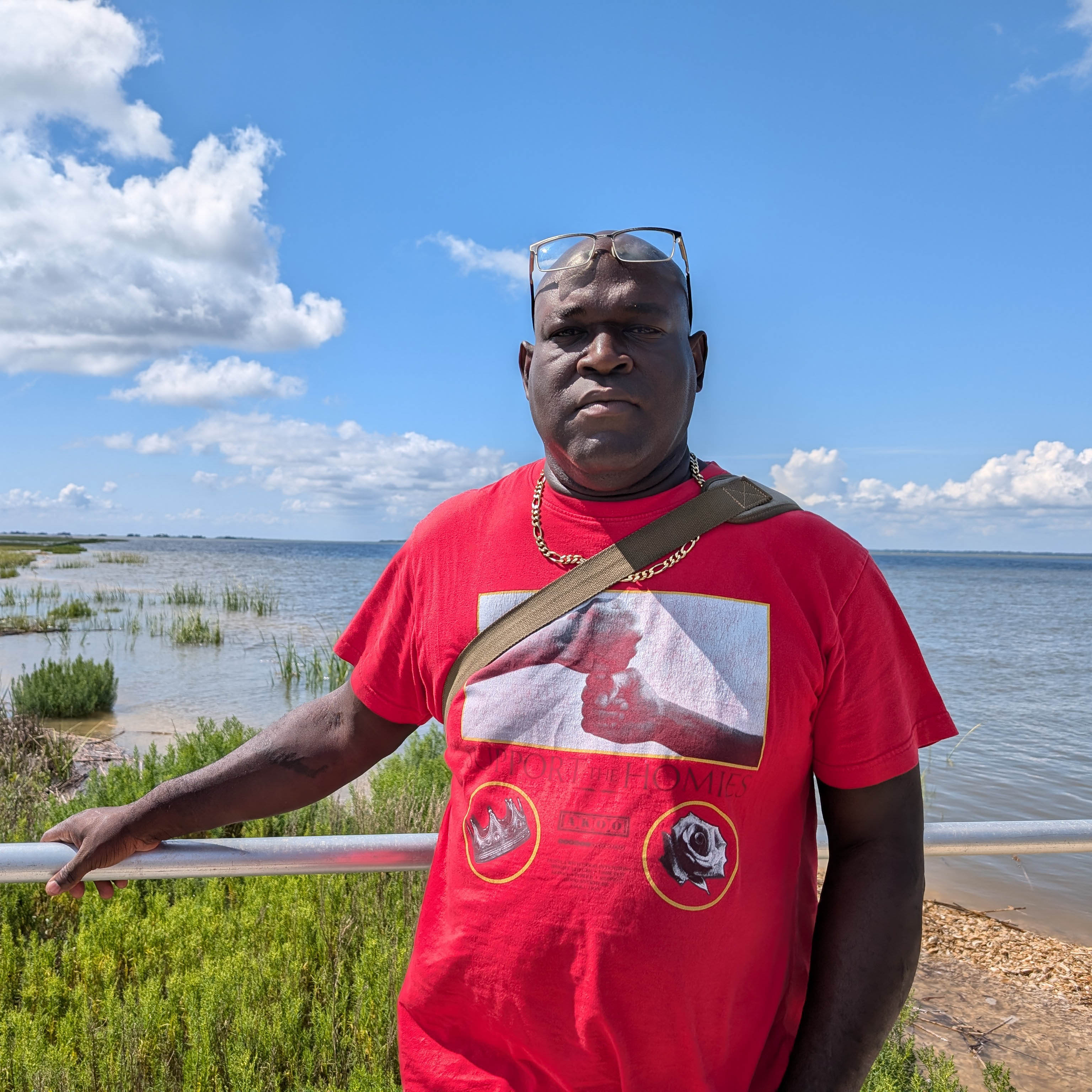 Person in red shirt stands outdoors along a shoreline.