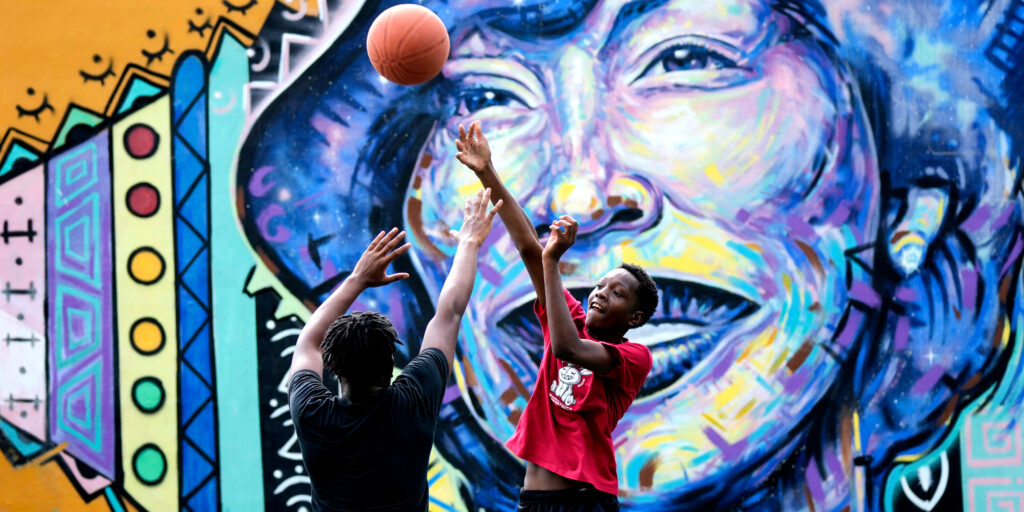 Two kids play basketball in front of a mural of Zoral Neale Hurston.