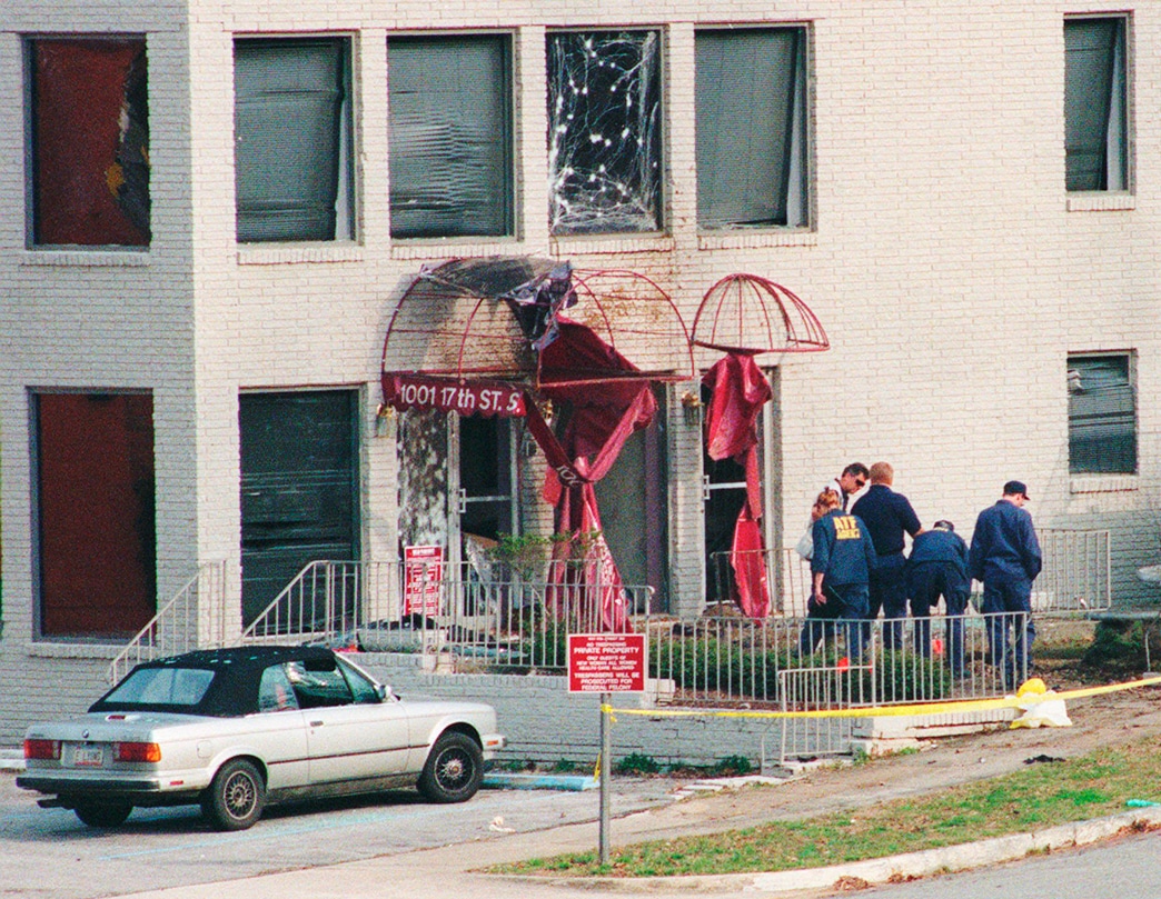 People outside a building that has a burned awning, broken window and other damage from bomb explosion.