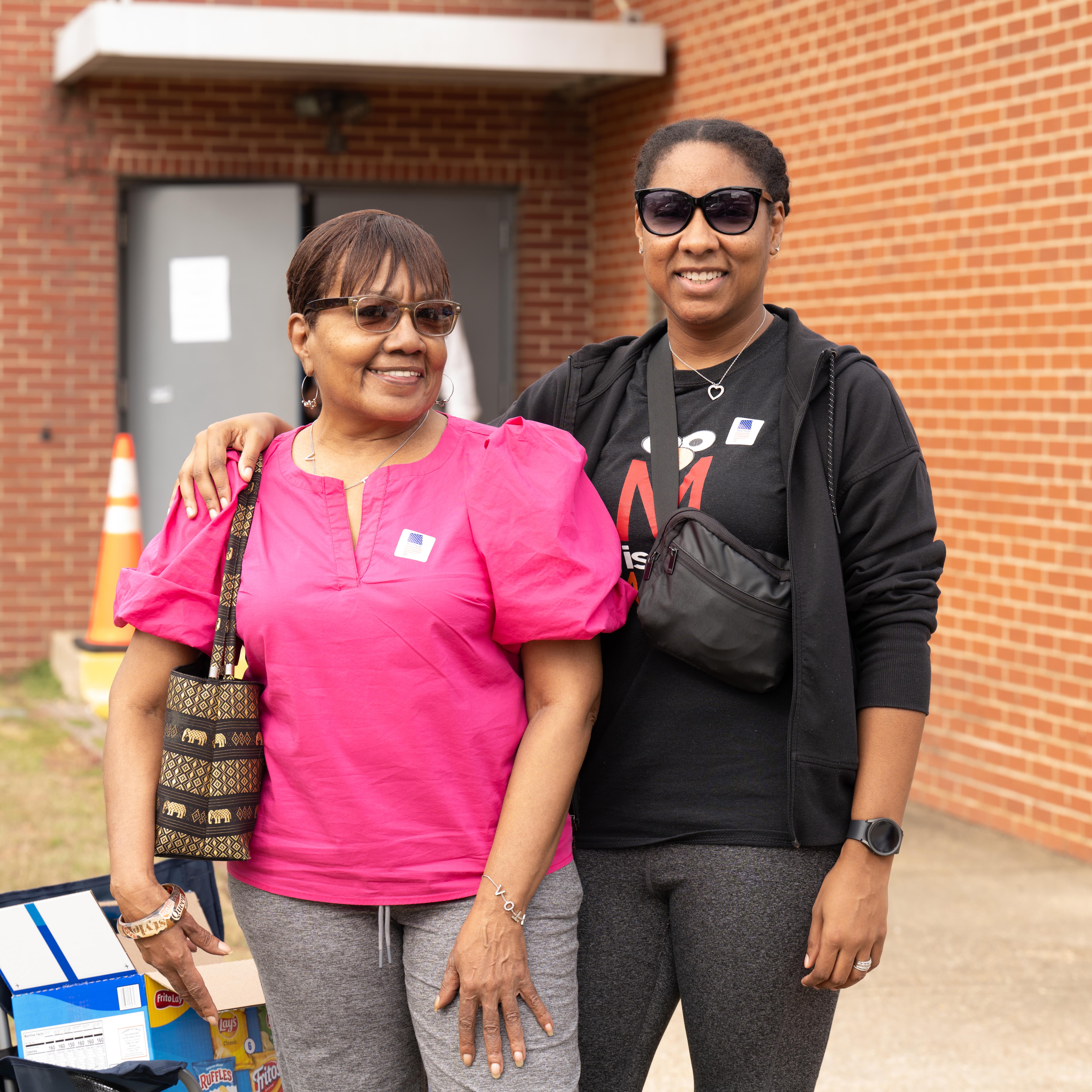 Two people pose next to each other outside.