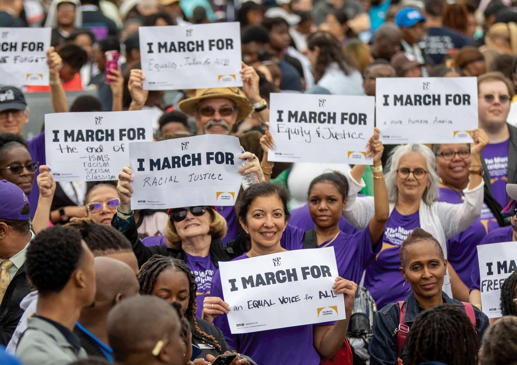 Crowd of people hold up signs that read "I March For ..."