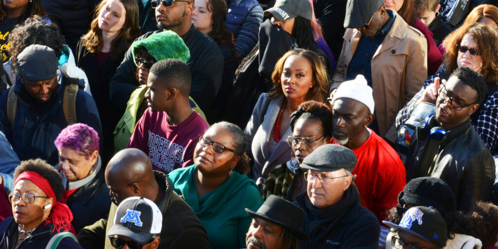 Crowd of marchers, with central young female figure making eye contact with the viewer.