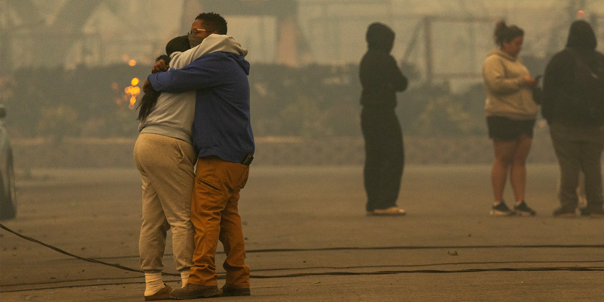 two people wearing masks embrace in a smog-filled city