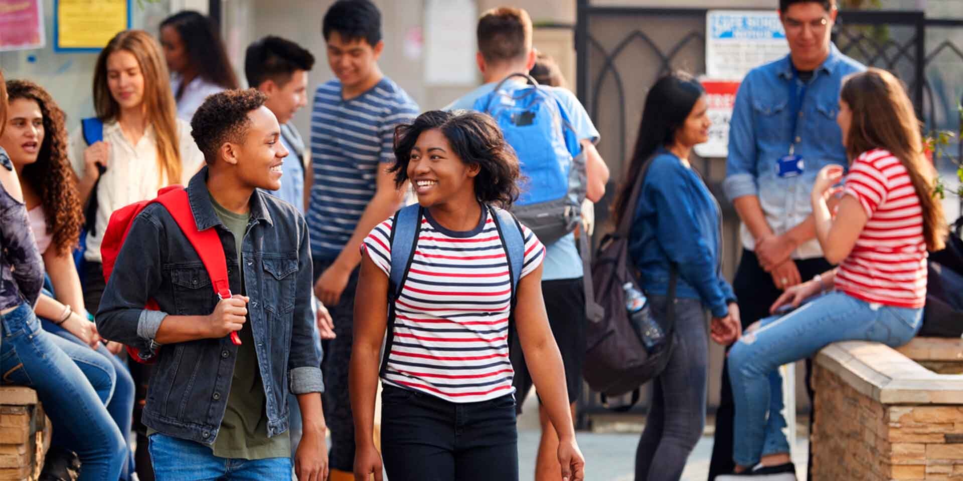 Group of schoolchildren with backpacks mill about in an exterior space.