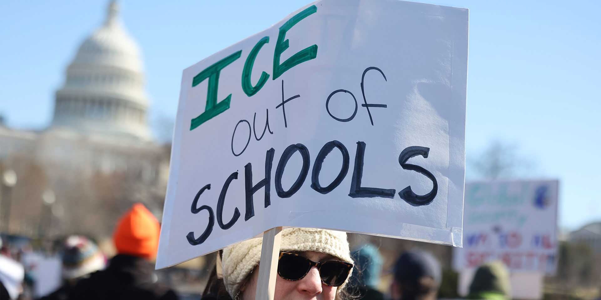 Una persona sostiene un cartel de papel que dice "ICE fuera de las escuelas" con el Capitolio de los EE. UU. de fondo.