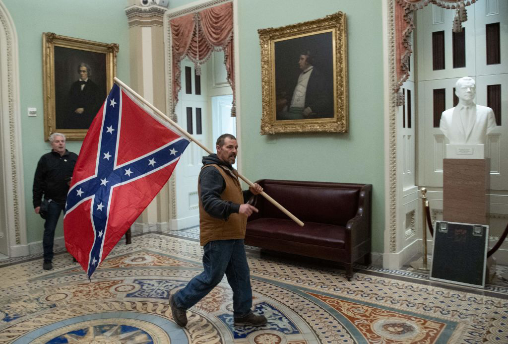 Person with flag on pole hanging from shoulder inside a large gallery.