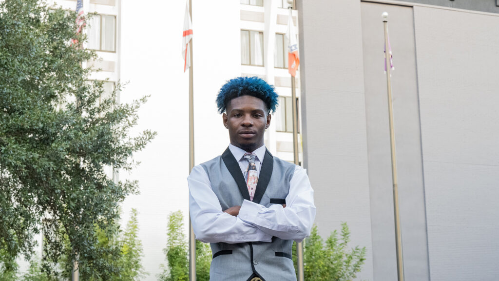 Person in exterior setting with two flag poles in background.