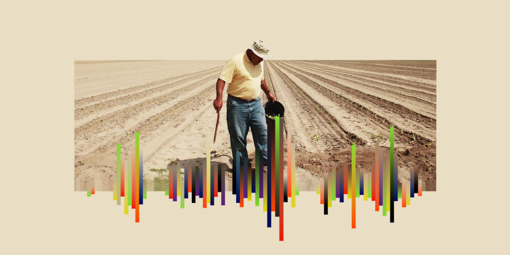 A farmer in a dirt field is holding a bucket and a stick.