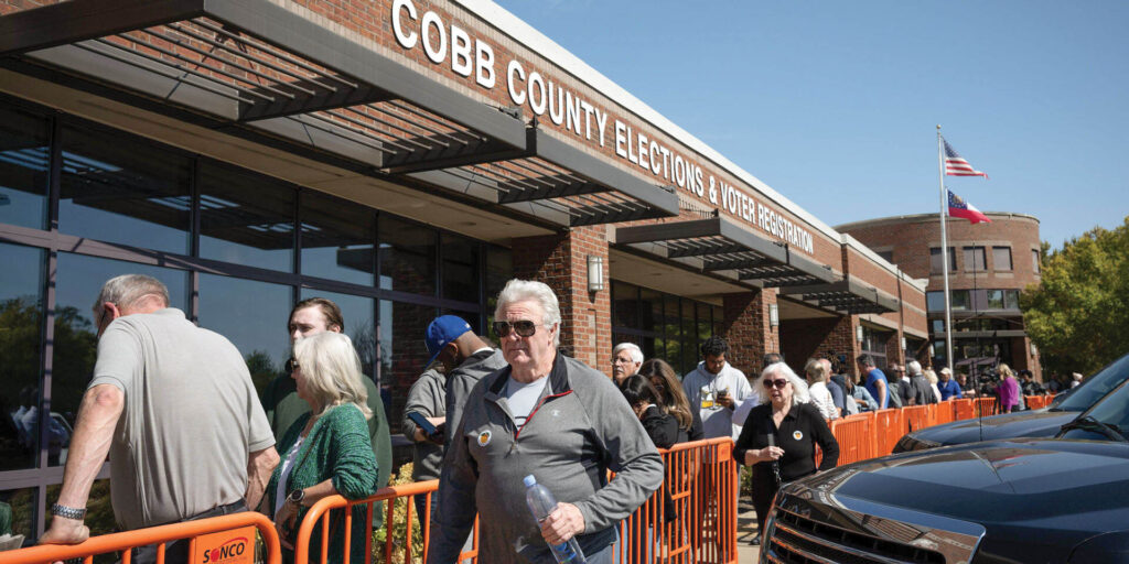 People lined up by barricade under an awning that reads: Cobb County Elections & Voter Registration.