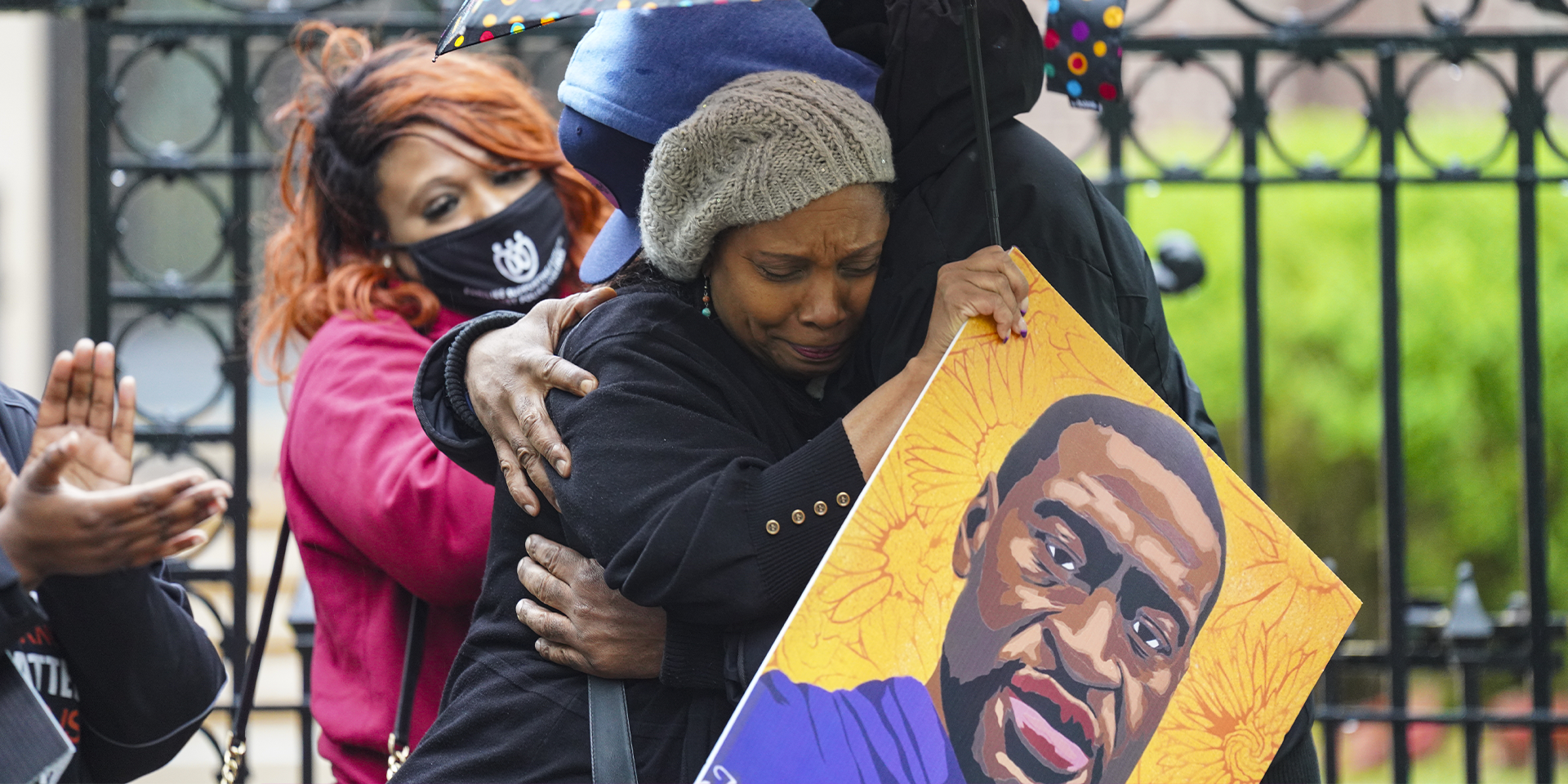 A group of protesters are hugging. One is carrying a portrait of George Floyd.