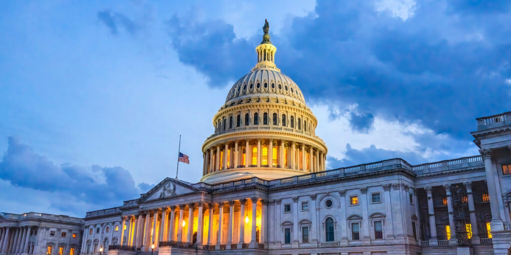US Capitol building illuminated by lights amid a darkening sky.