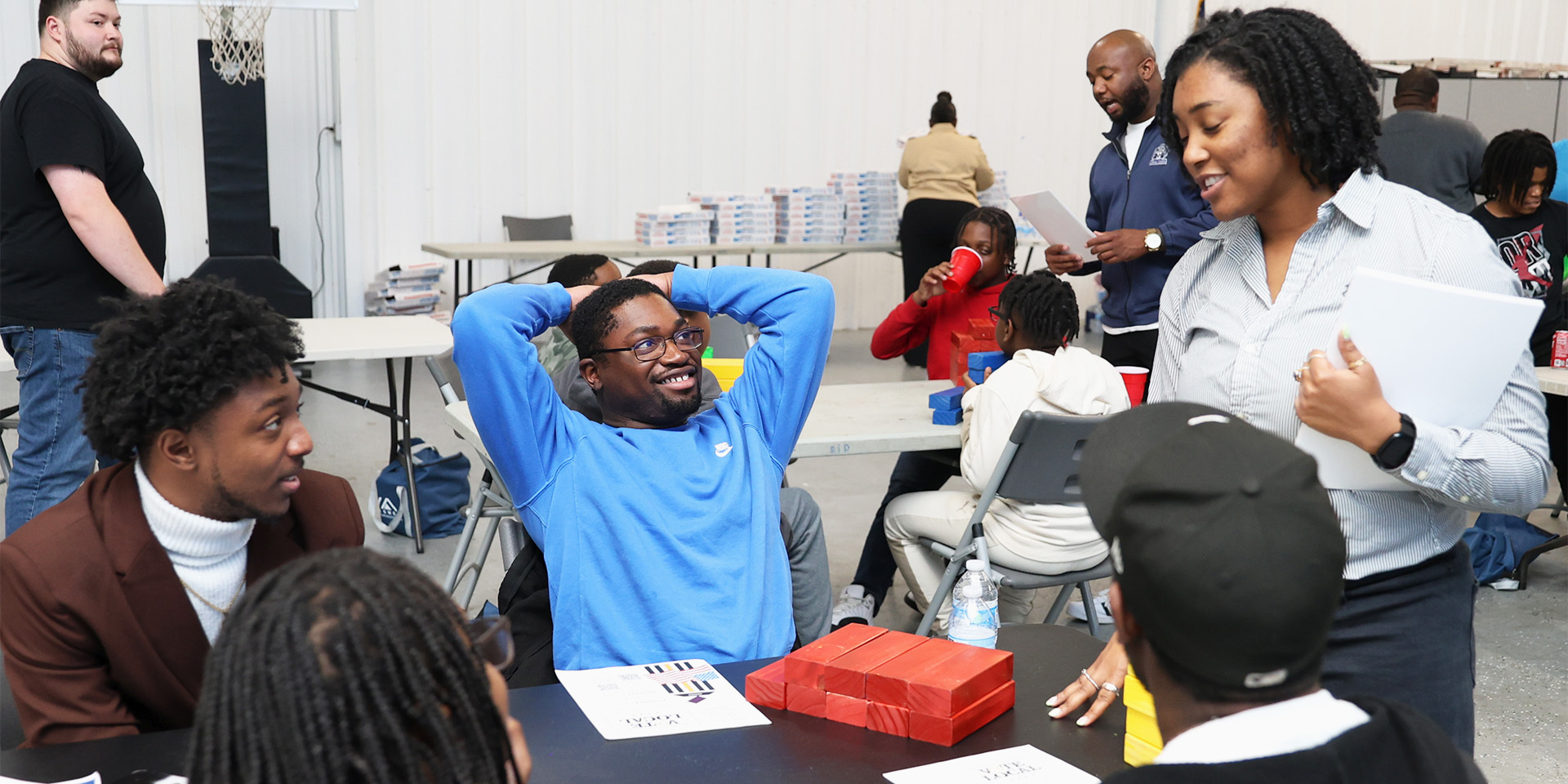 People interact at a table set to play a game with blocks and paper.