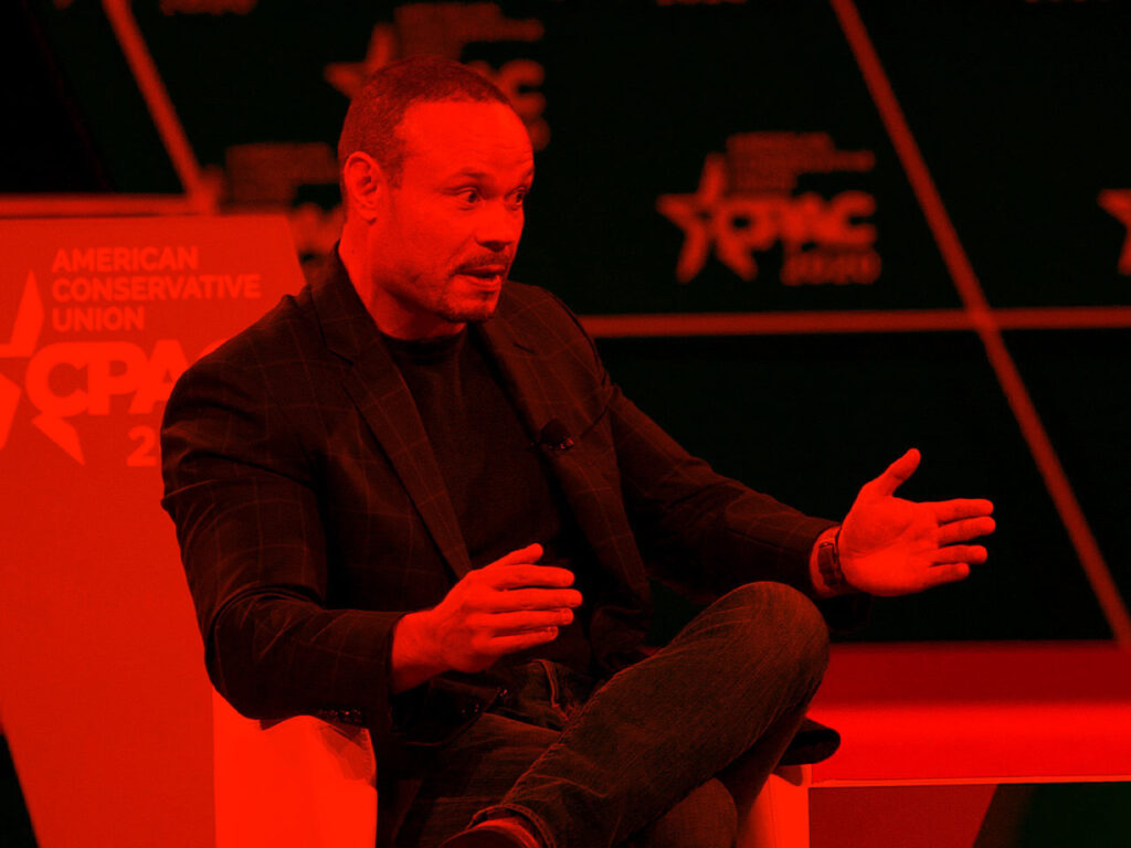 Figure seated on a stage with hands extended highlighted by a bright color.