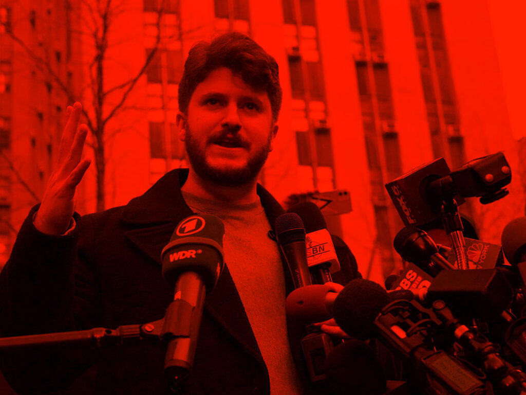 Person standing outside speaks into bank of microphones highlighted by vibrant color.