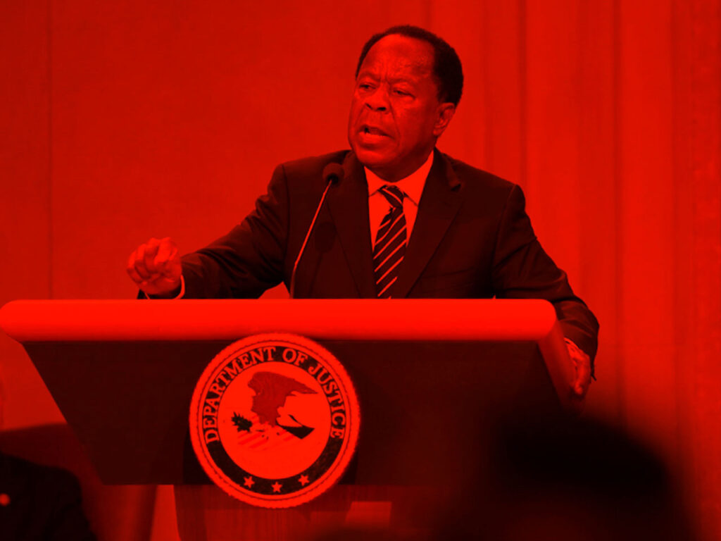 Person stands behind podium with governmental office seal highlighted by vibrant color.