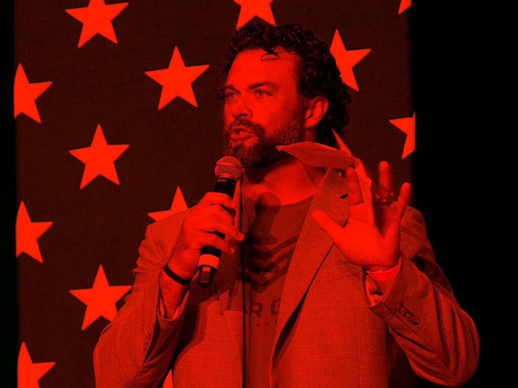Person holds microphone in front of US flag highlighted by vibrant color.