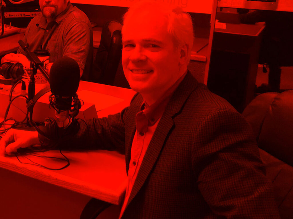Person turned away from microphone at desk highlighted by a vibrant color.