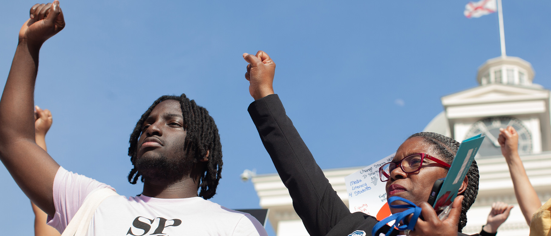 Two people stand outside the Alabama Capitol with raised fists. Their shirts read 'SPLC.'