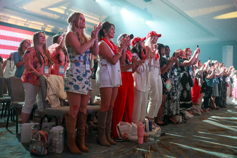 Crowd stands in applause with spotlights in background pointing toward forward stage.
