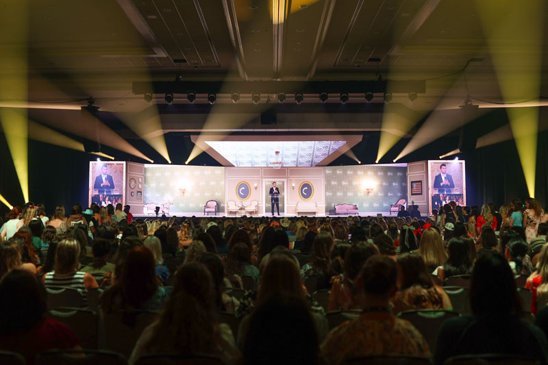Person at podium in front of crowd inside a ballroom.