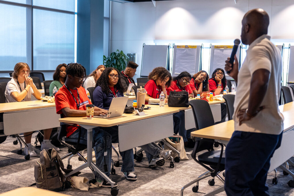 A man in with a microphone speaks to students in a classroom.