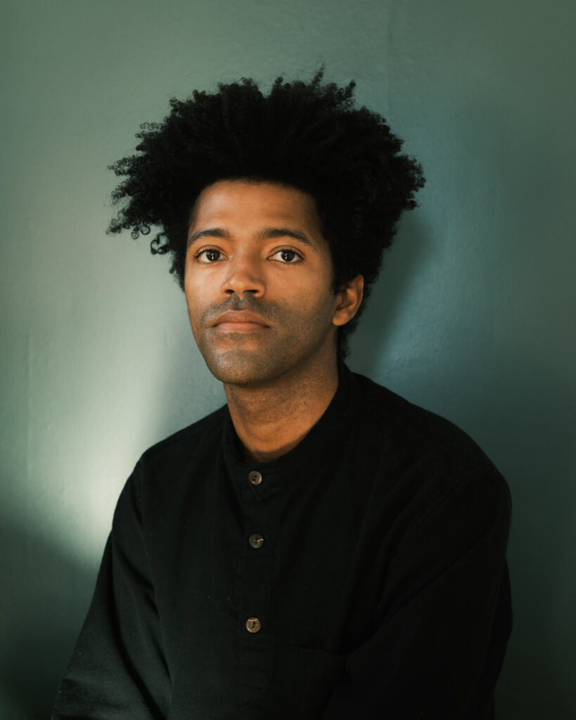 Headshot of a man in a black shirt against a green background.