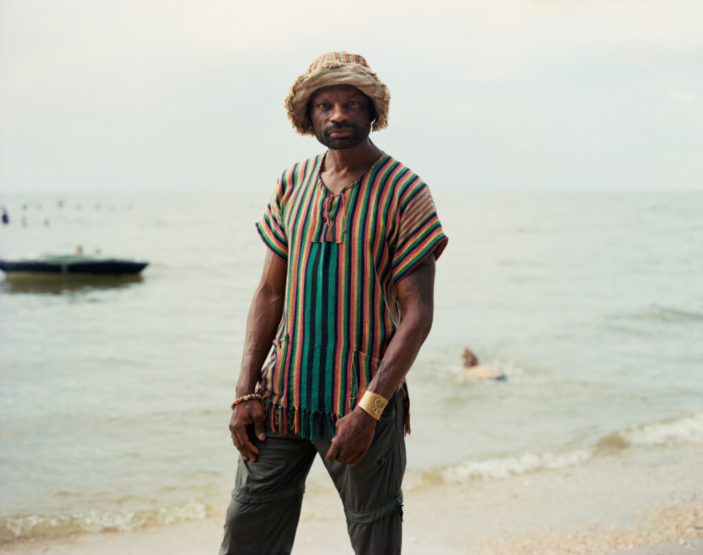 Man on a beach wearing a straw hat and colorful shirt with vertical stripes.