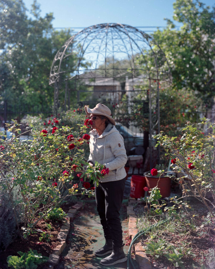Person in a white coat stands in a garden smelling roses.