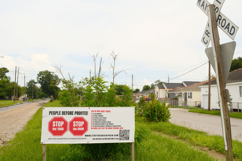 A grassy area separating a street is marked by a sign that opposes corporate pollution.