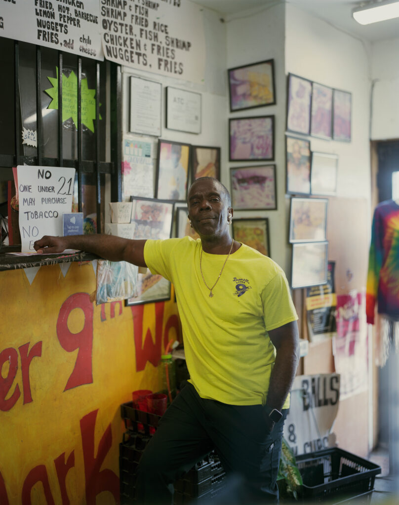 Man in a yellow shirt leaning on the counter of a convenience store.