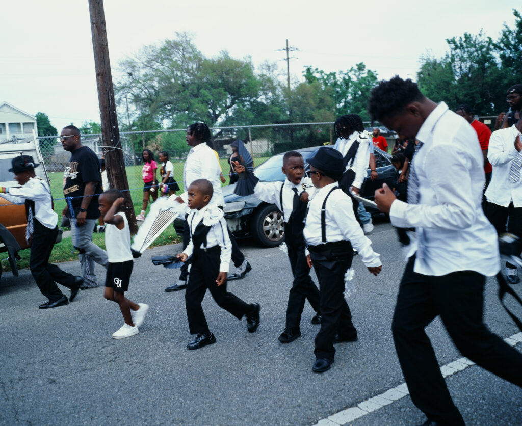 A group of children in white shirts and black pants mark down the street.