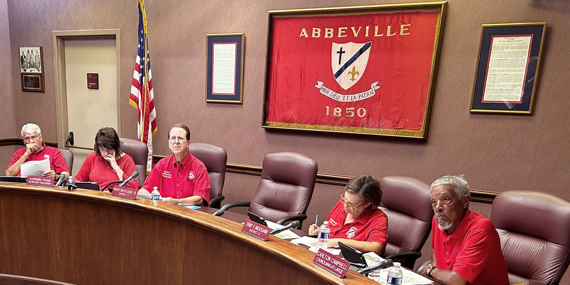 Abbeville city flag serves as background to half circle table with seated council members.