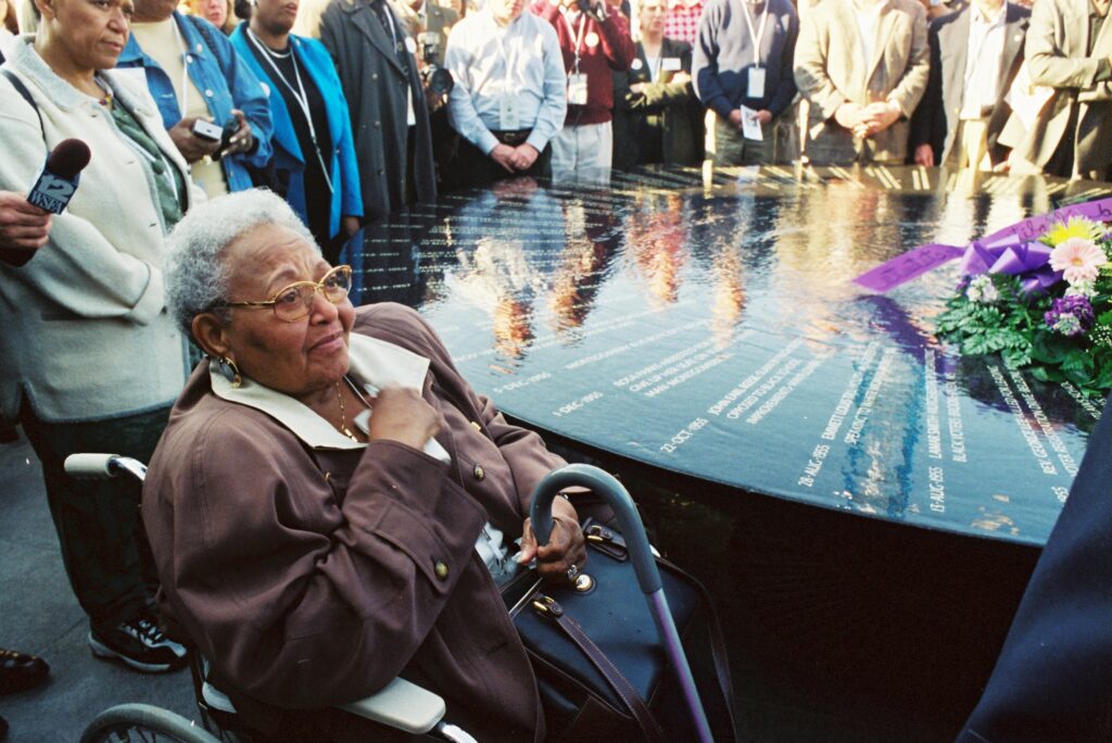 Person in wheelchair in foreground with other people surrounding a memorial.
